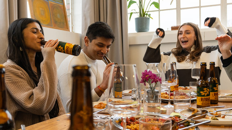 Friends sitting around a dining table, eating and drinking Barhi date-based mead during a lively meal.