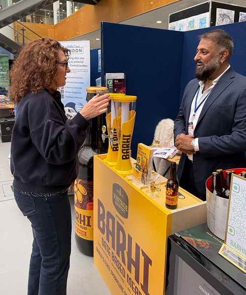 A woman sampling Barhi date-based mead while speaking with a Barhi representative at a branded expo stand.