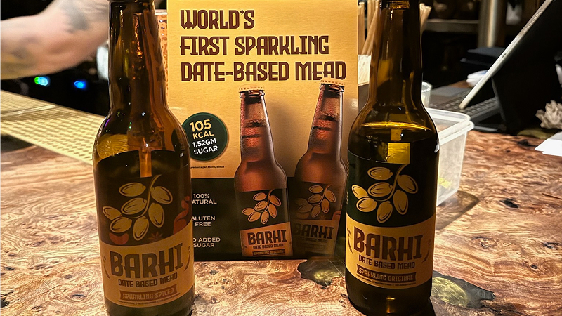 Barhi sparkling date-based mead bottles displayed on a bar counter beside a sign reading - World's First Sparkling Date-Based Mead.