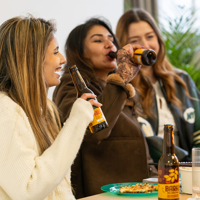 Friends enjoying Barhi date-based mead together indoors, sharing drinks and food in a relaxed setting.
