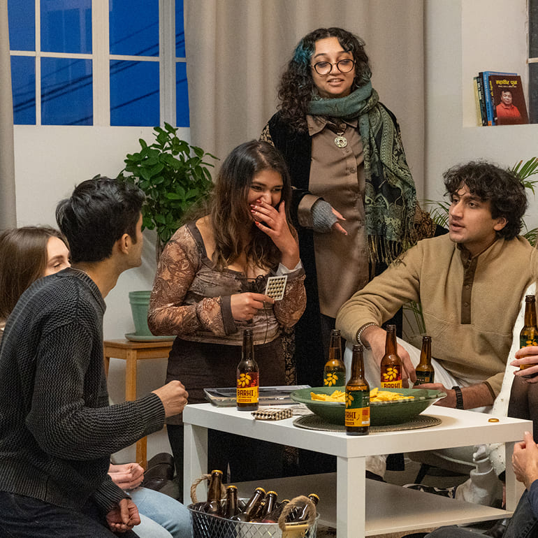 Group of friends gathered around a table at a house party, drinking Barhi date-based mead and playing games.