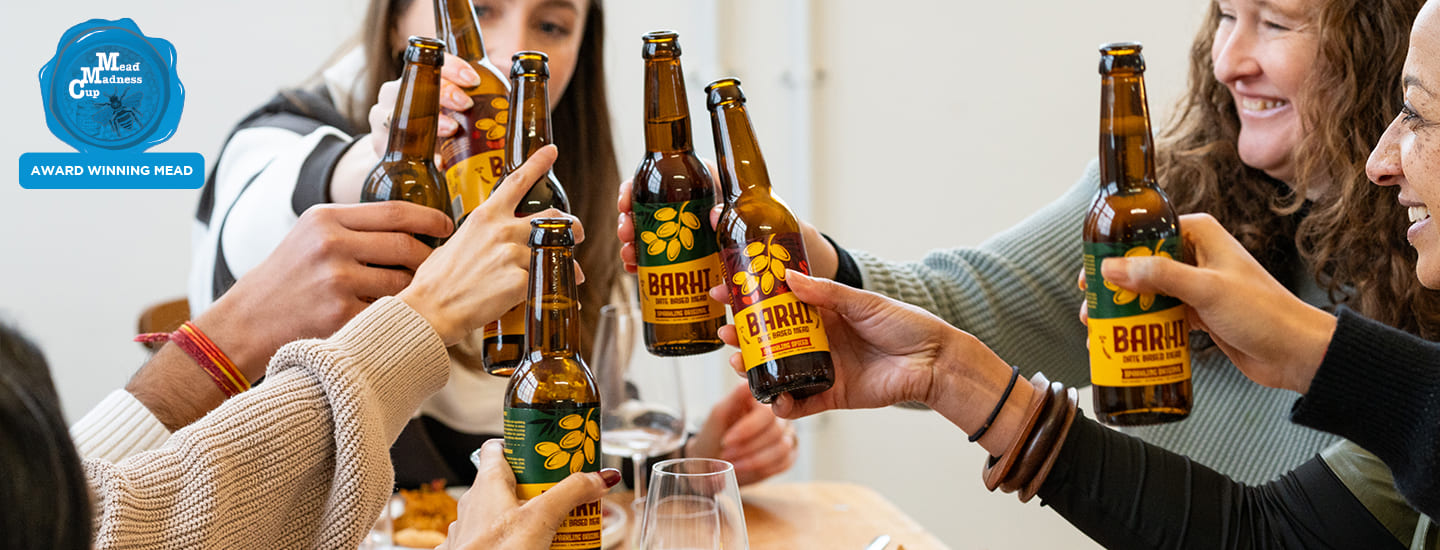 Group of friends raising Barhi date-based mead bottles together in a celebratory toast indoors.