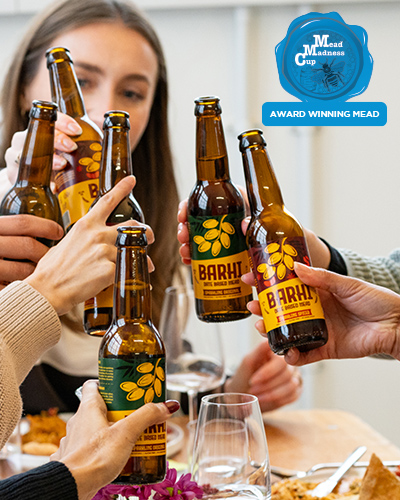 Group of friends raising Barhi date-based mead bottles together in a celebratory toast indoors.