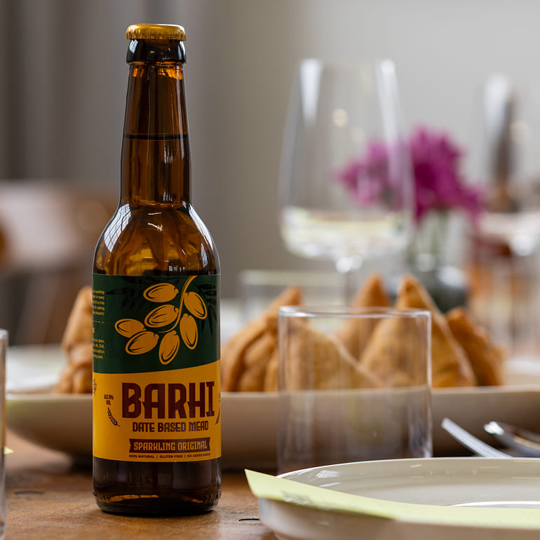 A bottle of Barhi sparkling date-based mead on a dining table set with plates, glasses, and fried appetizers