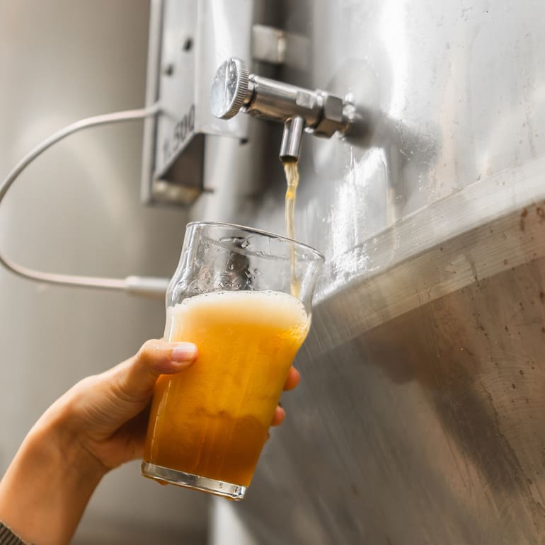 Freshly brewed date-based mead being poured from a stainless steel fermentation tank into a glass