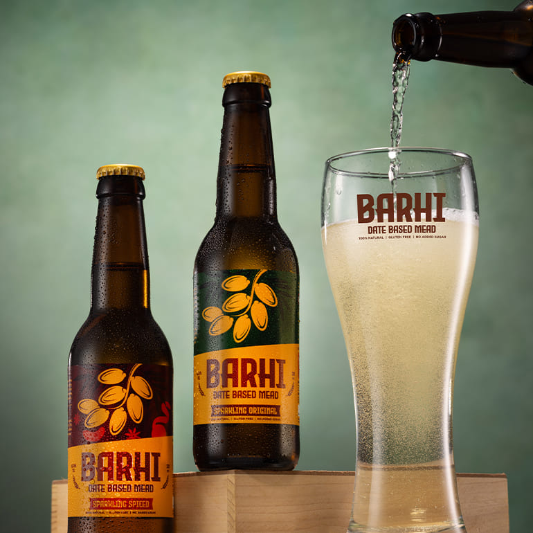 Barhi date-based sparkling mead poured into a branded glass alongside bottled products
