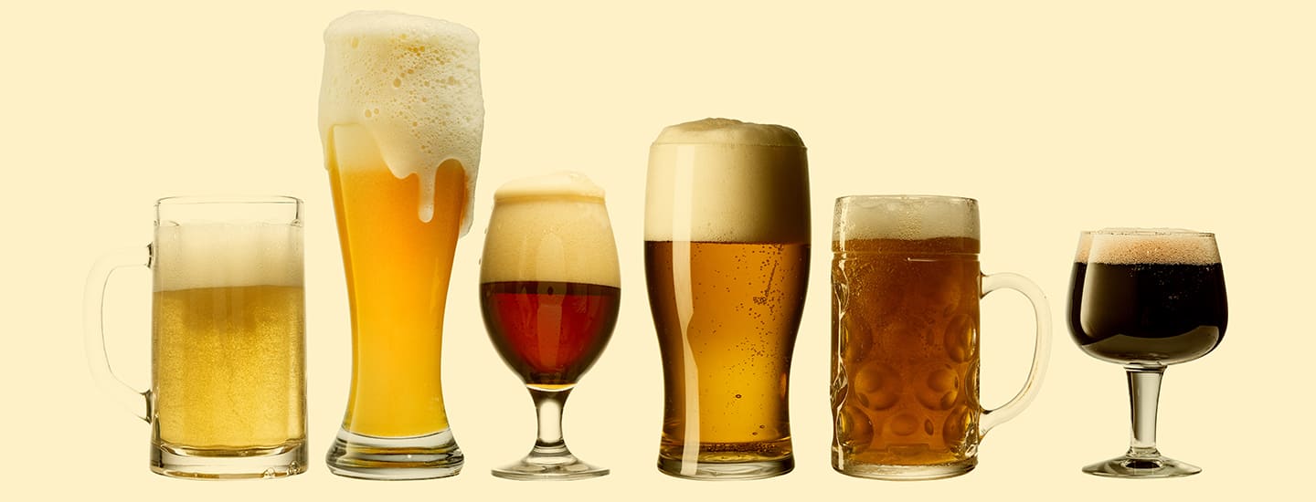 Row of different beer, wine mead glasses filled with light and dark beverages against a neutral background