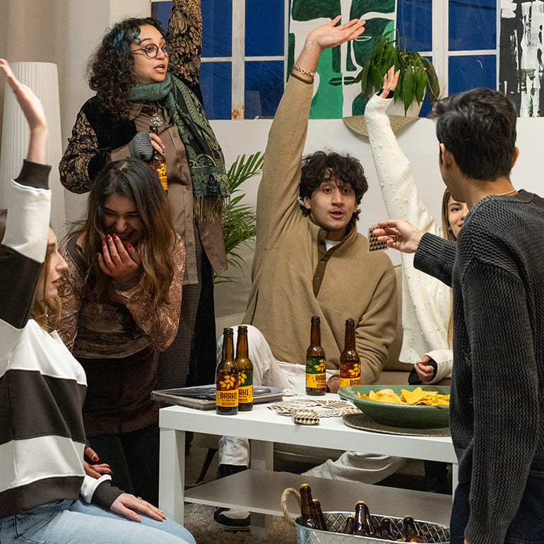 Group of friends gathered around a table at a house party, drinking Barhi date-based mead and playing games.