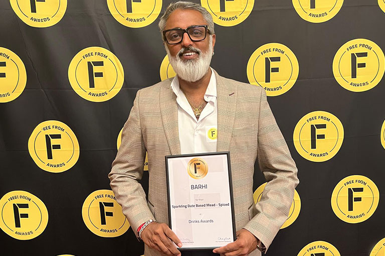 Barhi founder Vikas Thakker holding award certificate for BARHI Sparkling Date Based Mead – Spiced featuring Free From Awards backdrop