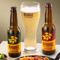 Two bottles of BARHI date-based beverage with a frosty glass of in the centre, styled alongside Indian food